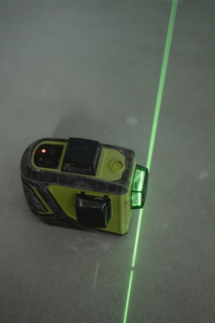 A green cross-line laser level on a concrete floor projecting a green line