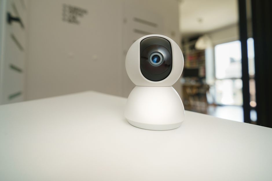 A small white pan-and-tilt indoor security camera on a white table in a flat