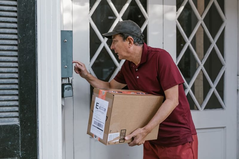 A delivery man holding a parcel and pressing a buzzer beside a glazed front door
