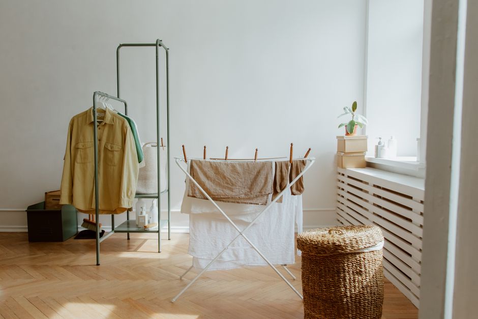 Laundry drying on a white airer indoors beside a clothes rail and a wicker basket