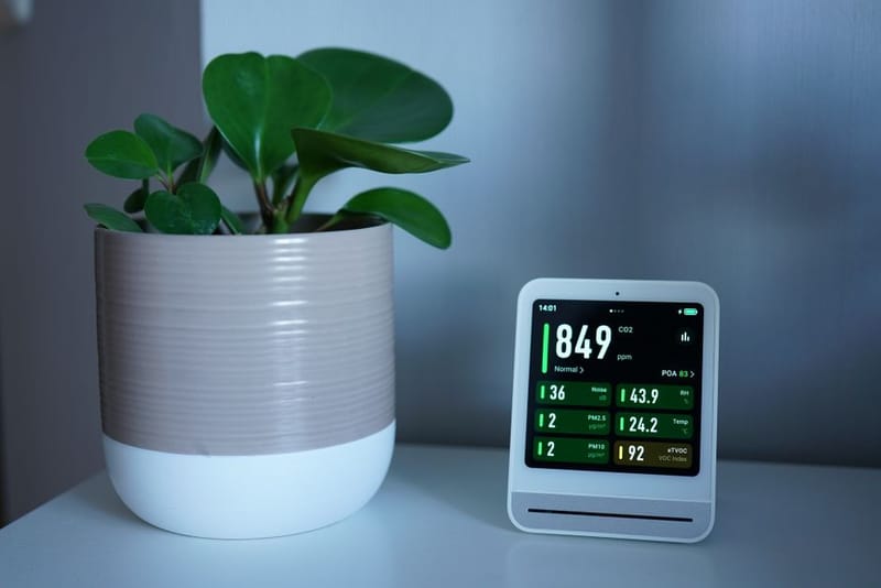 An air quality monitor showing a CO2 reading of 849 ppm beside a potted plant