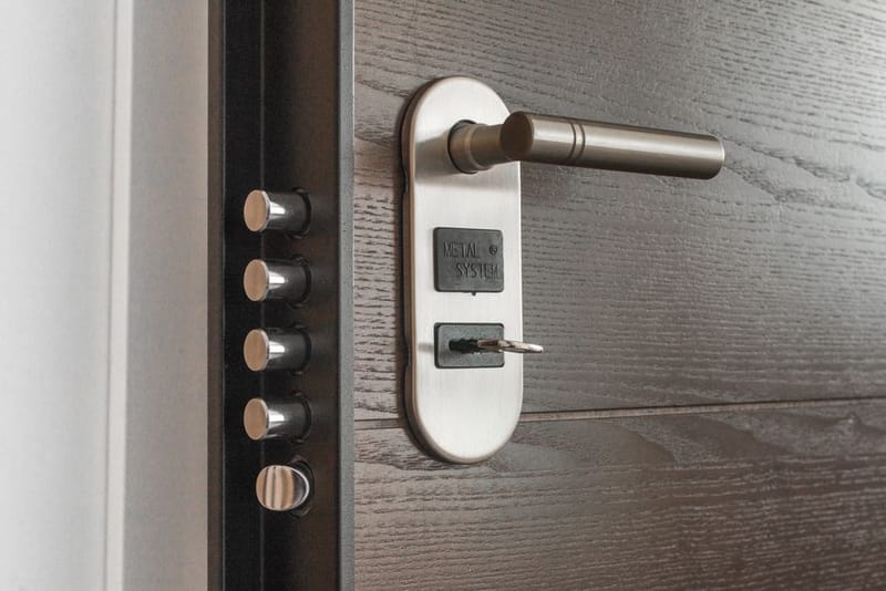 A security door's edge with five steel locking bolts beside a lever handle and key