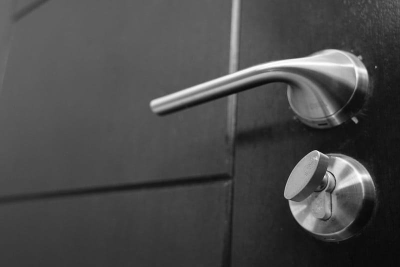 Black-and-white close-up of a lever handle and a lock thumb-turn on a dark door