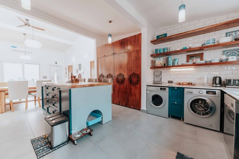 A kitchen with two washing machines under open shelves and a wooden island with a cat-litter nook